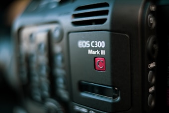 Close-up of a professional video camera, showcasing the EOS C300 Mark III model insignia. The focus is on the branding, with partial views of buttons and controls in the blurred background.