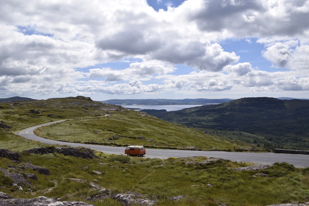 Coche rojo en un campo de hierba verde bajo nubes blancas durante el día