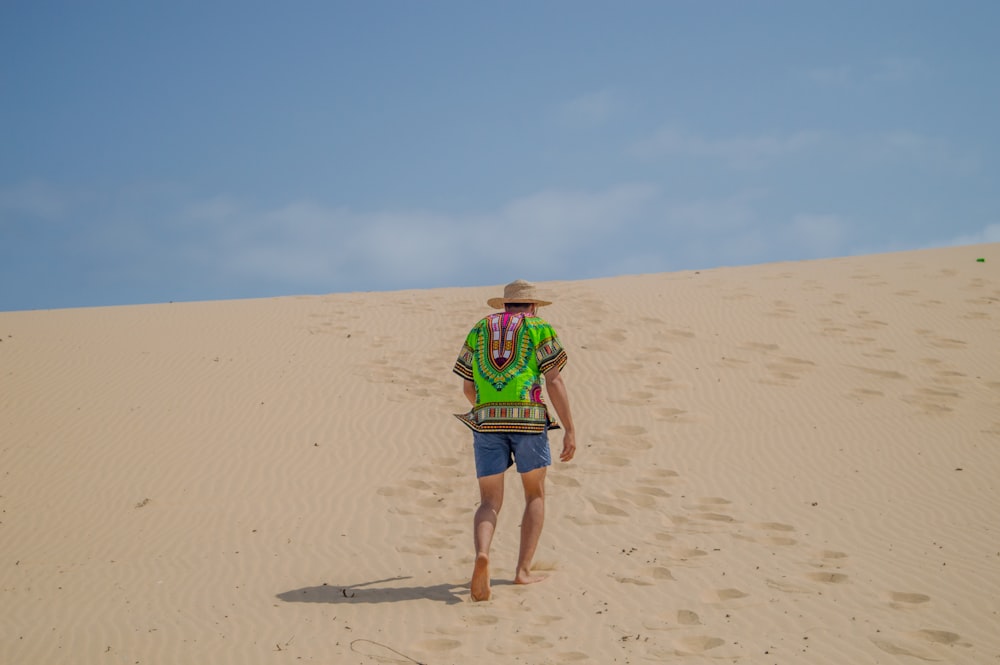 woman in green shirt and blue denim shorts walking on brown sand during daytime