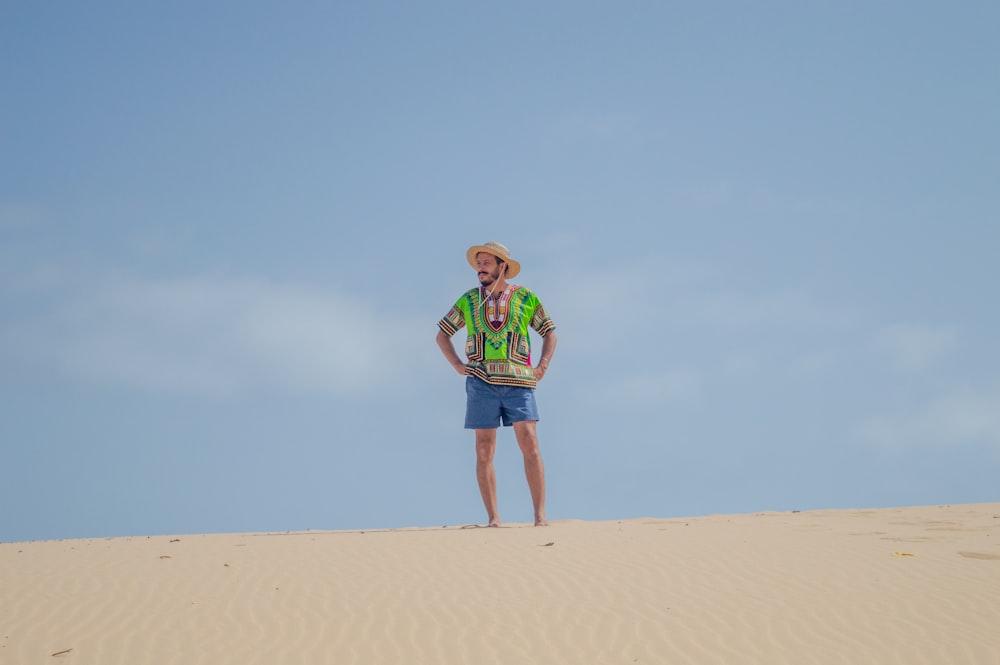 man in green shirt and blue shorts walking on brown sand during daytime