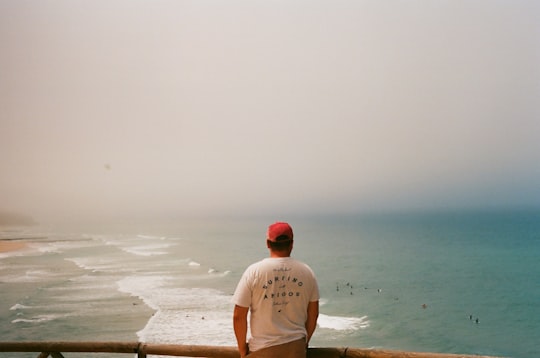 man in white crew neck t-shirt standing on beach during daytime in Arrifana Portugal