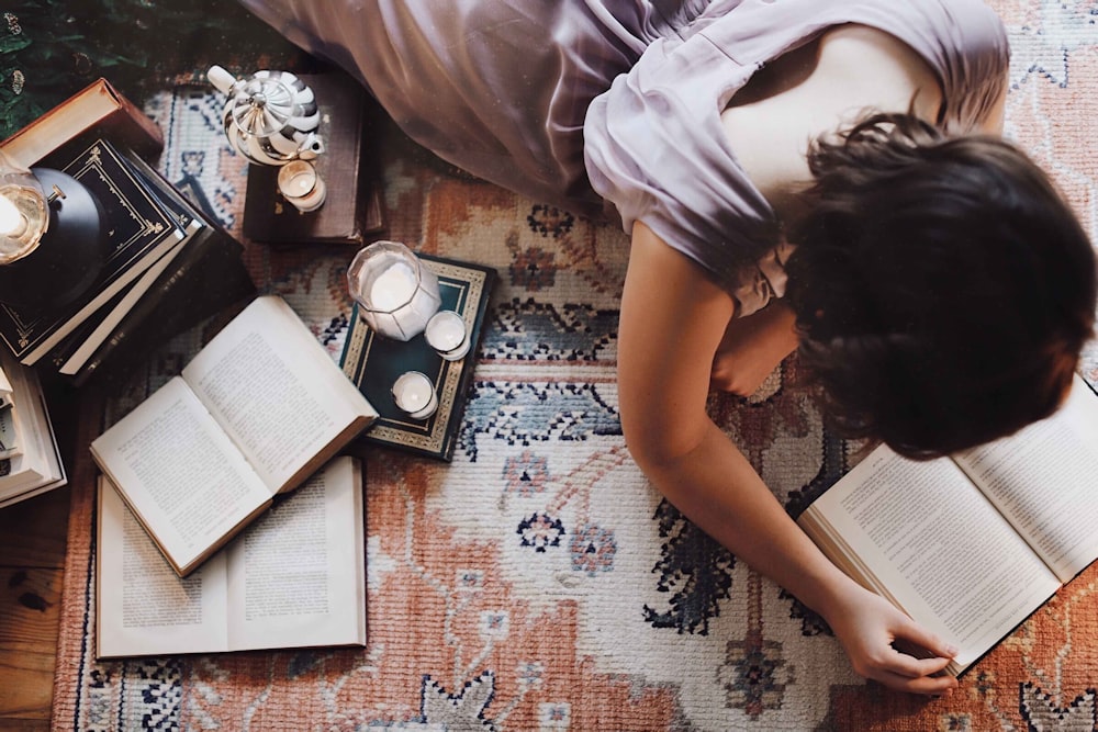 Mujer con camiseta blanca tirada en el suelo con libros y fotos