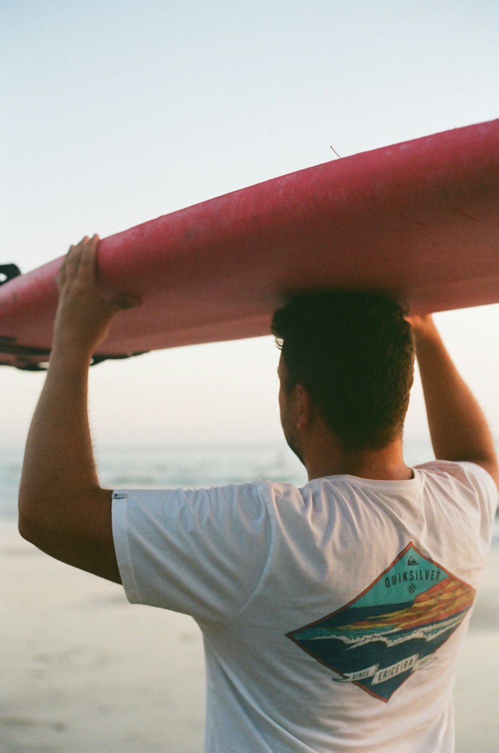man in white t-shirt holding red surfboard during daytime