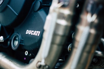 Close-up view of a Ducati motorcycle engine with visible pipes and mechanical parts. The engine casing is prominently displaying the 'Ducati' logo.