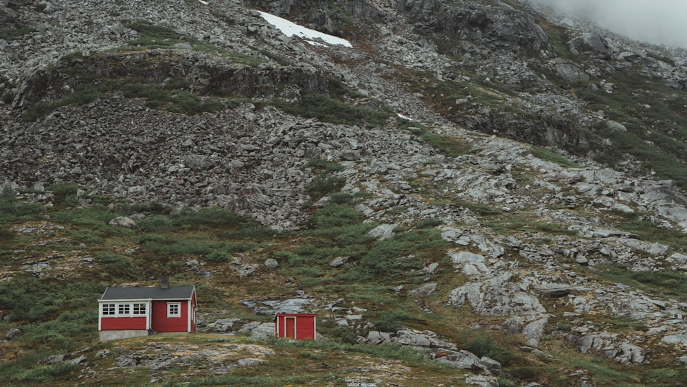 casa vermelha e branca no campo de grama verde perto da montanha rochosa durante o dia