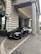 A luxury car is parked in front of an ornate, historic building with large stone columns. The vehicle is sleek and modern, painted in a matte black shade. The entrance to the building features a green awning and decorative stonework.