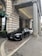 A luxury car is parked in front of an ornate, historic building with large stone columns. The vehicle is sleek and modern, painted in a matte black shade. The entrance to the building features a green awning and decorative stonework.