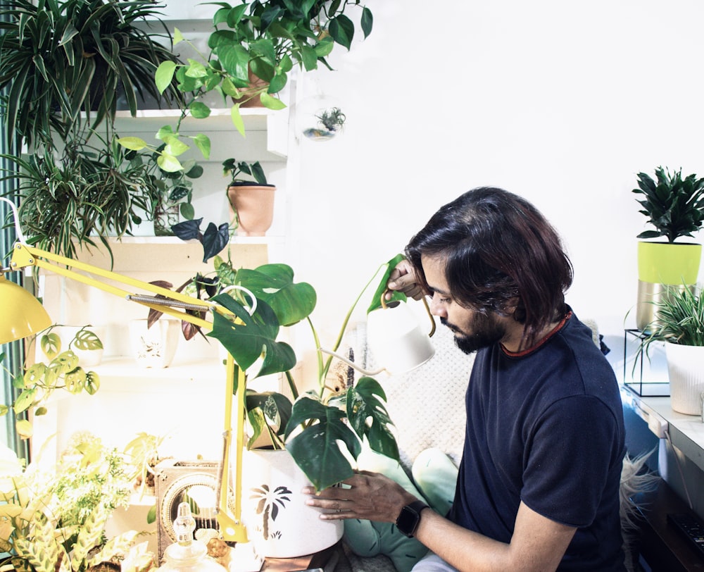 man in blue crew neck t-shirt sitting beside green plant