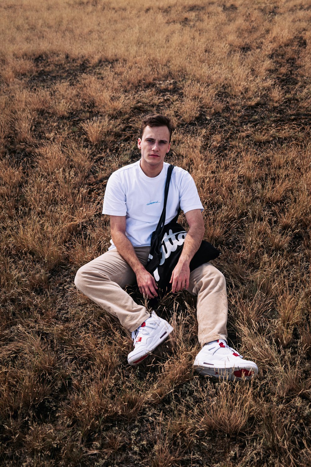 man in white crew neck t-shirt and brown pants sitting on brown grass field