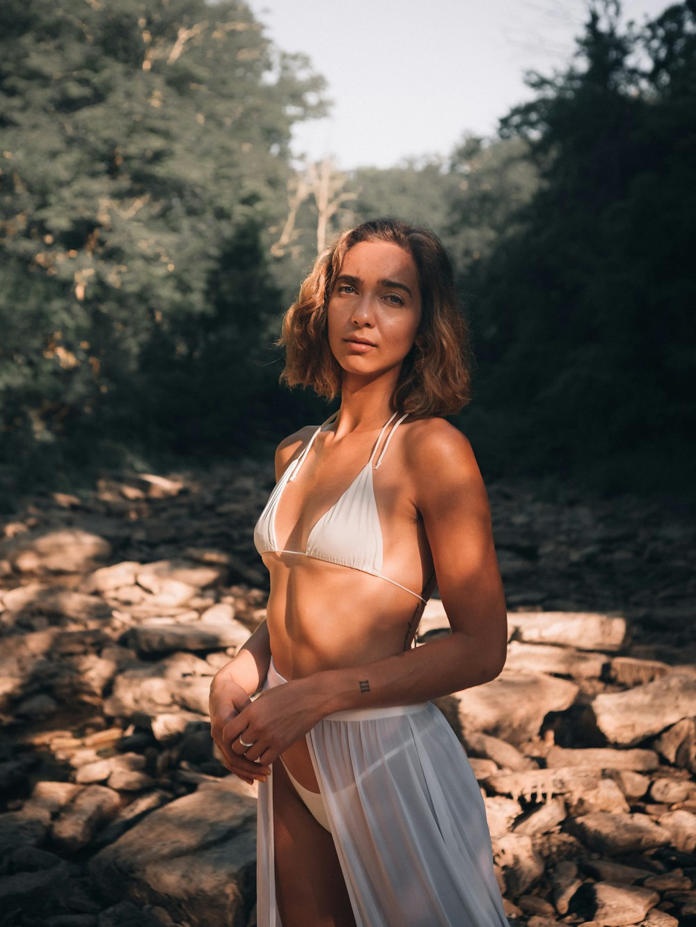 woman in white spaghetti strap top and blue denim shorts standing on brown sand during daytime