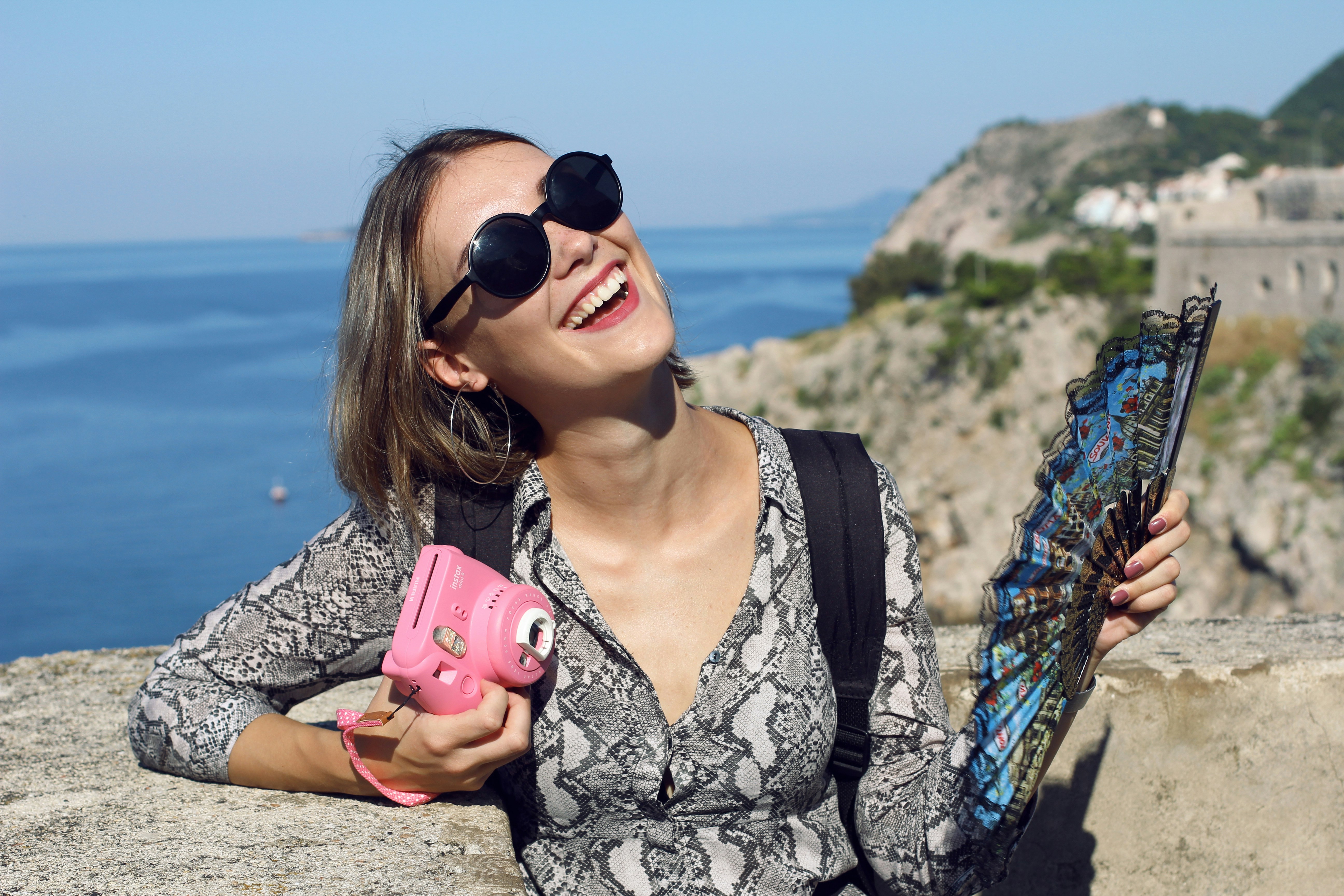 Woman in black and white floral shirt holding pink smartphone