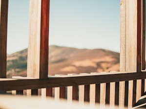 A serene terrace view overlooking rolling hills and distant sea, framed by natural wood railings and soft off-white walls.