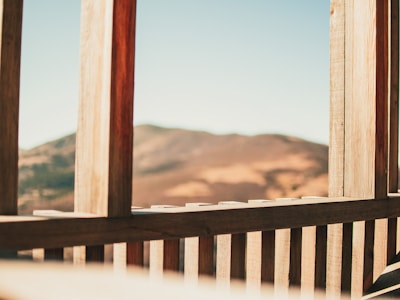 A serene terrace view overlooking rolling hills and distant sea, framed by natural wood railings and soft off-white walls.