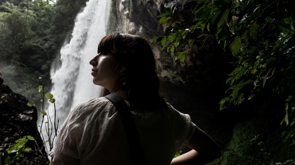 woman in brown shirt standing near waterfalls during daytime