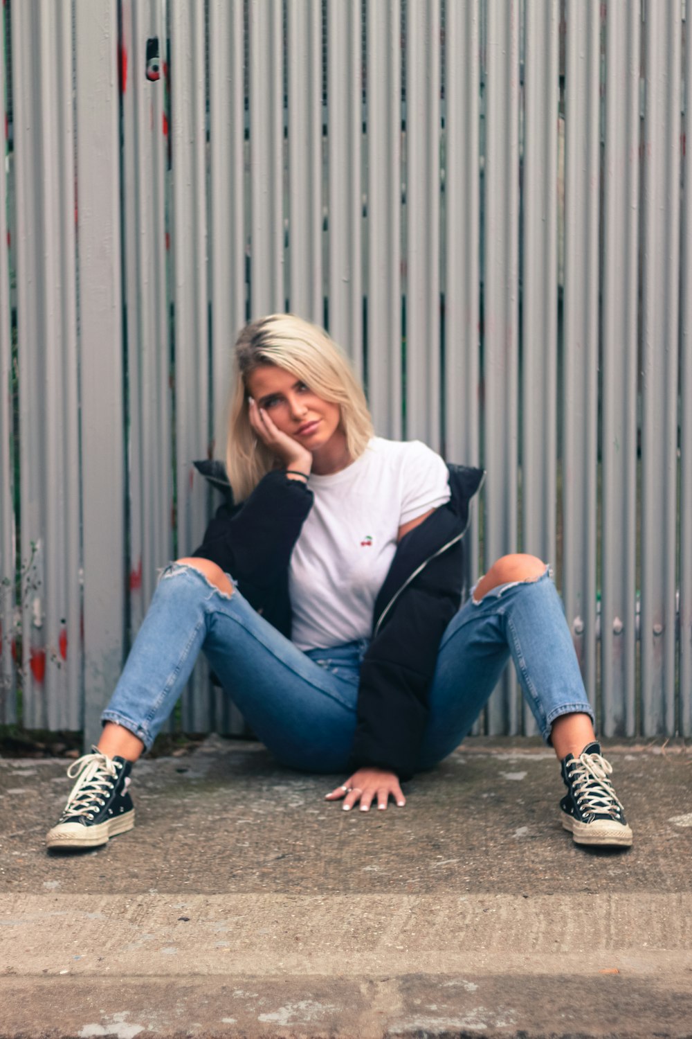 woman in white long sleeve shirt and blue denim jeans sitting on gray wooden fence