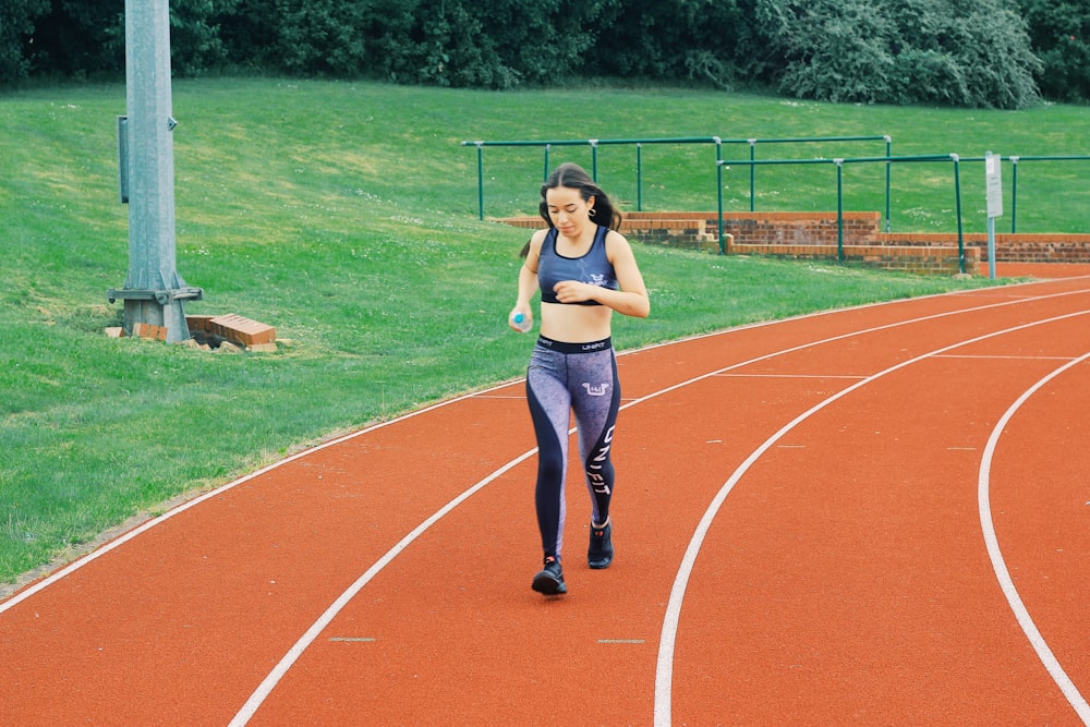 黒いスポーツブラと青いデニムジーンズを着た女性が昼間に陸上競技場に立つ