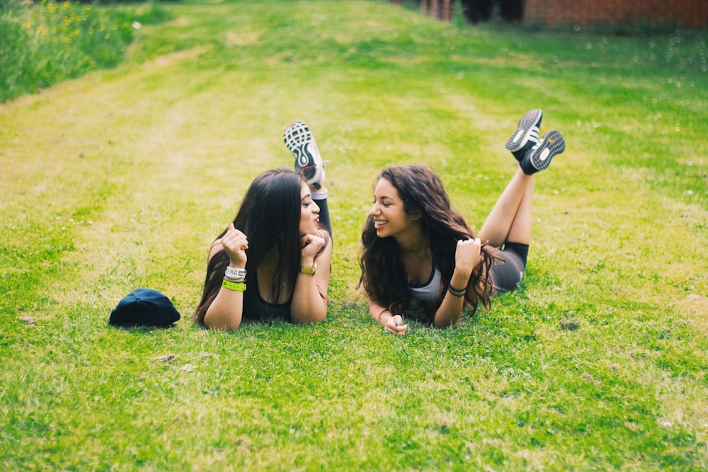 2 women lying on green grass field during daytime