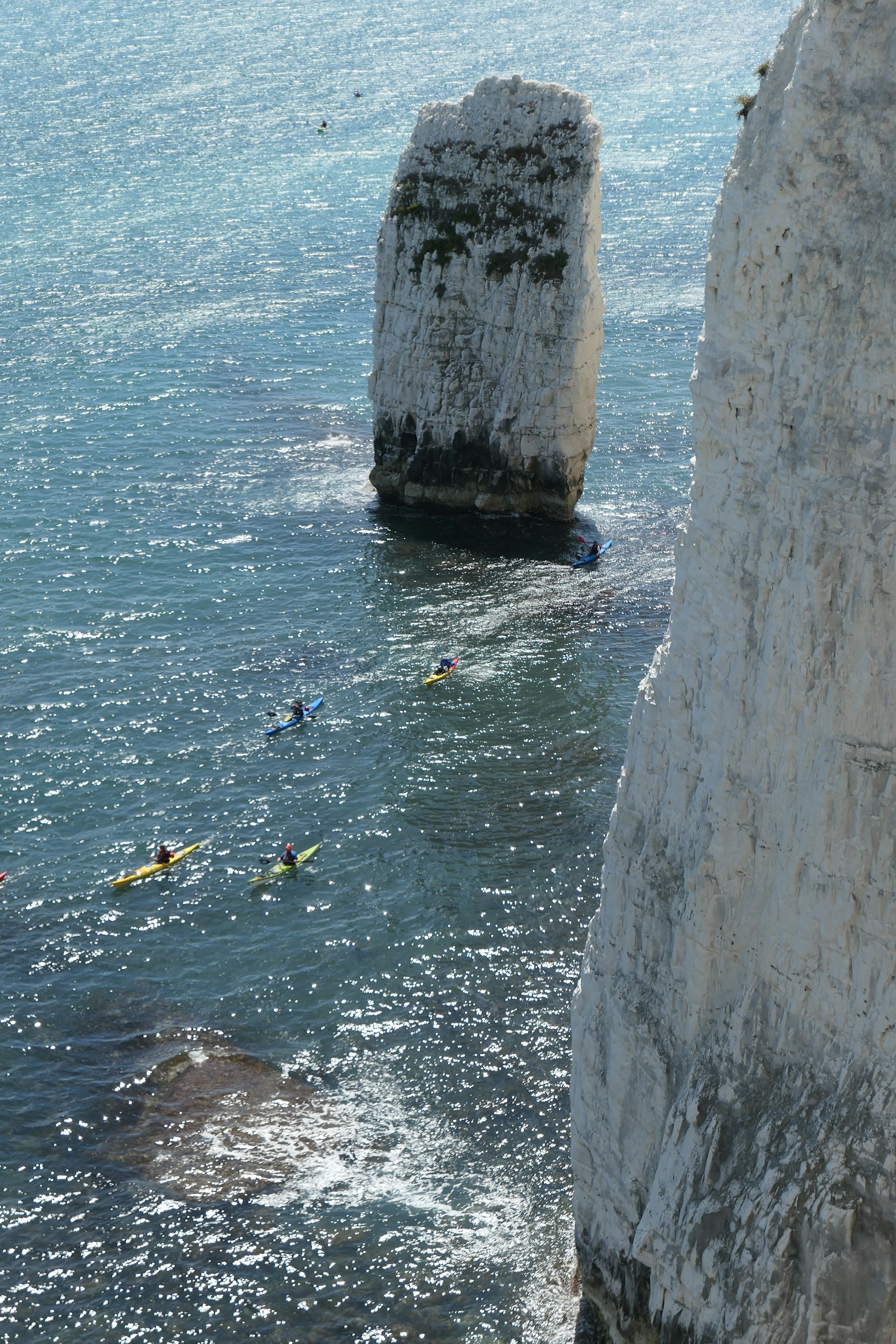 A group of travelers kayaking through a hidden lagoon surrounded by towering green cliffs under a bright blue sky.