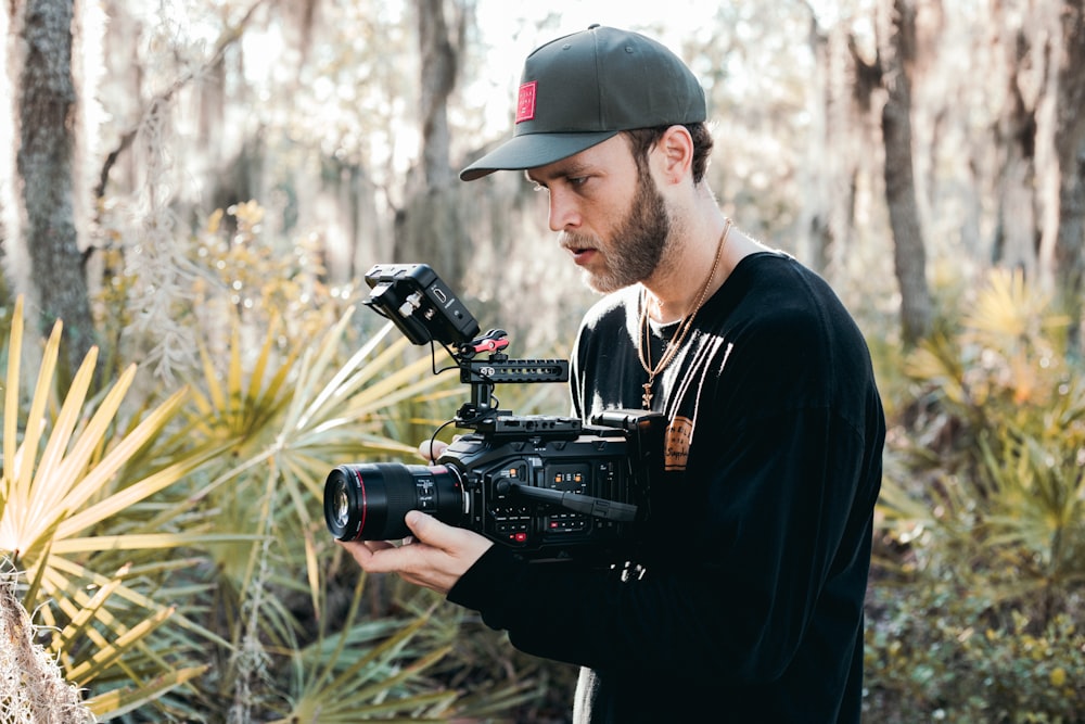 man in black hat holding black dslr camera