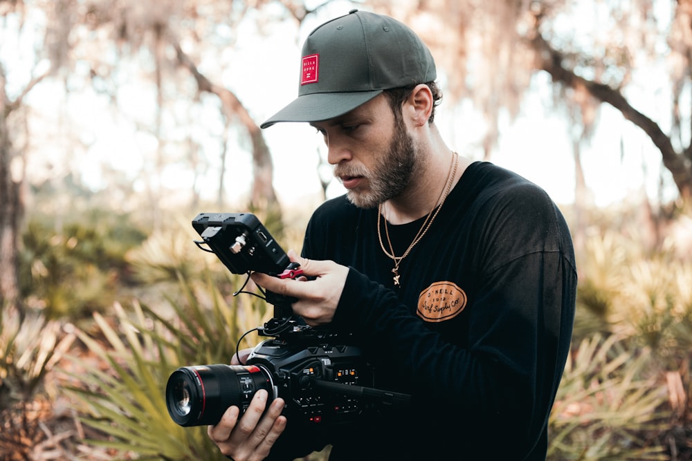 uomo in t-shirt girocollo nera che tiene la fotocamera DSLR nera