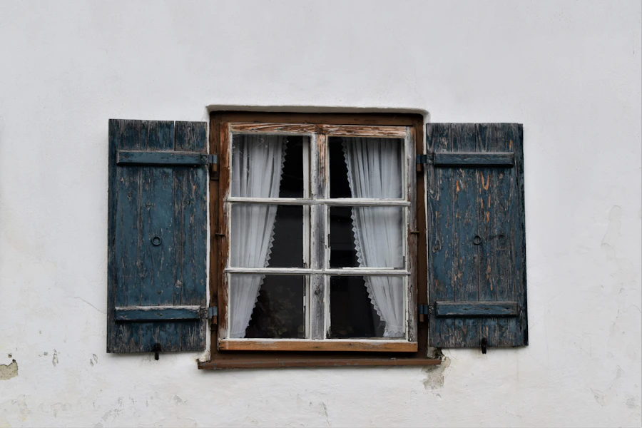 Altes Holzfenster mit Sprossen und Klappläden an einer weißen Hausfassade
