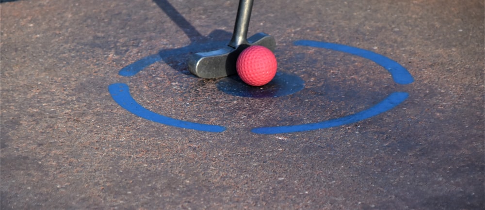 Pelota de golf roja sobre pavimento de hormigón marrón y blanco