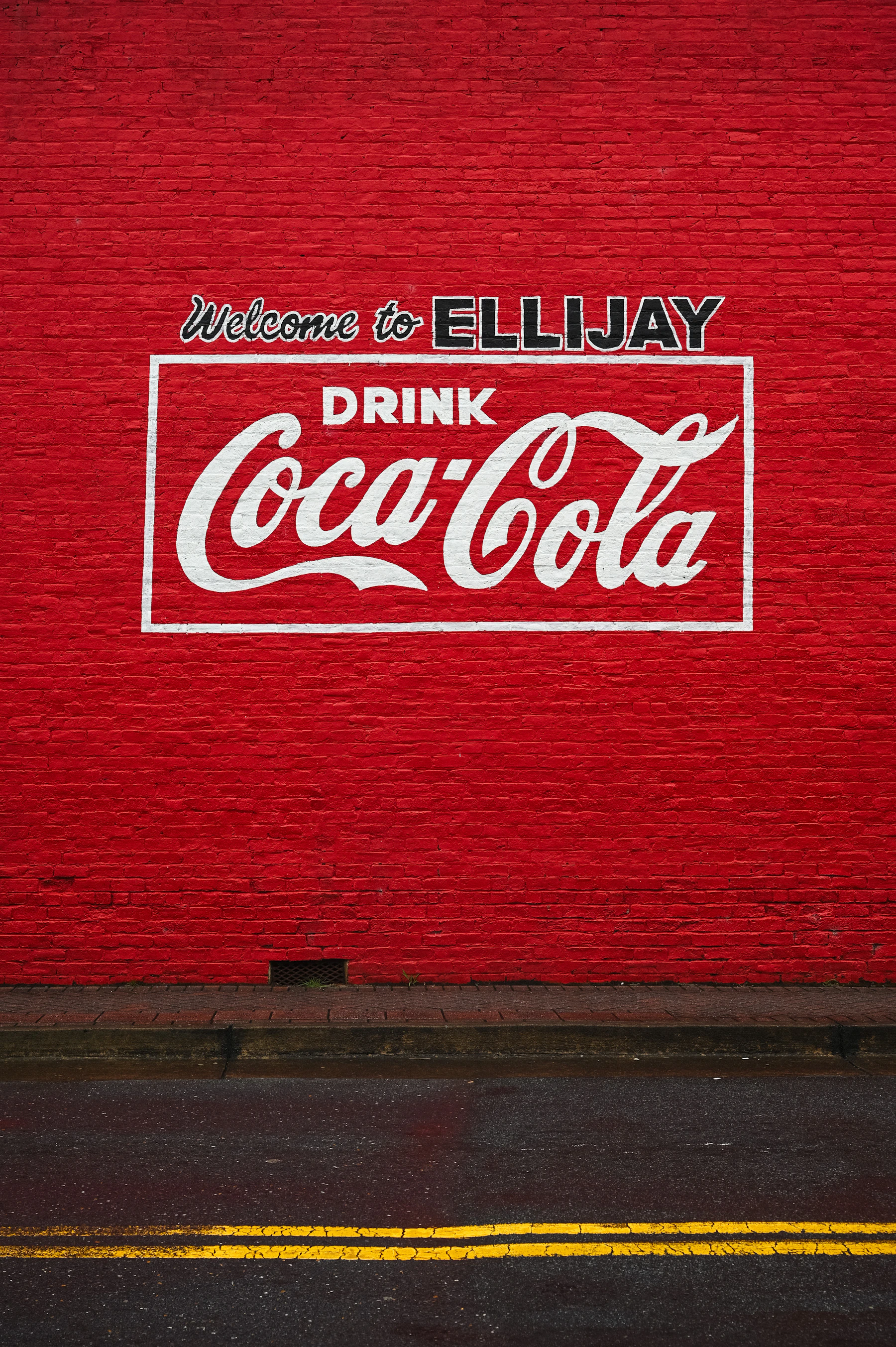 A red brick wall painted with a white Drink Coca-Cola sign