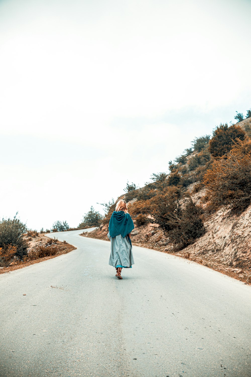 Frau in blauer Jacke geht tagsüber auf der grauen Straße spazieren
