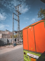 A bright orange mototaxi parked near a busy city corner with a clear blue sky.