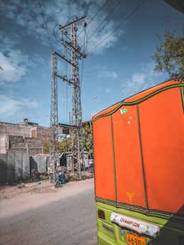 A bright orange mototaxi parked near a busy city corner with a clear blue sky.