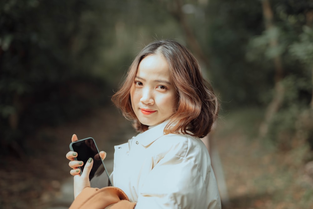 woman in white button up shirt holding black smartphone