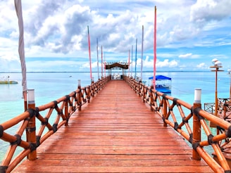 brown wooden bridge over blue sea under white clouds during daytime