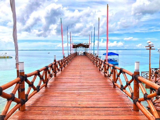 brown wooden bridge over blue sea under white clouds during daytime