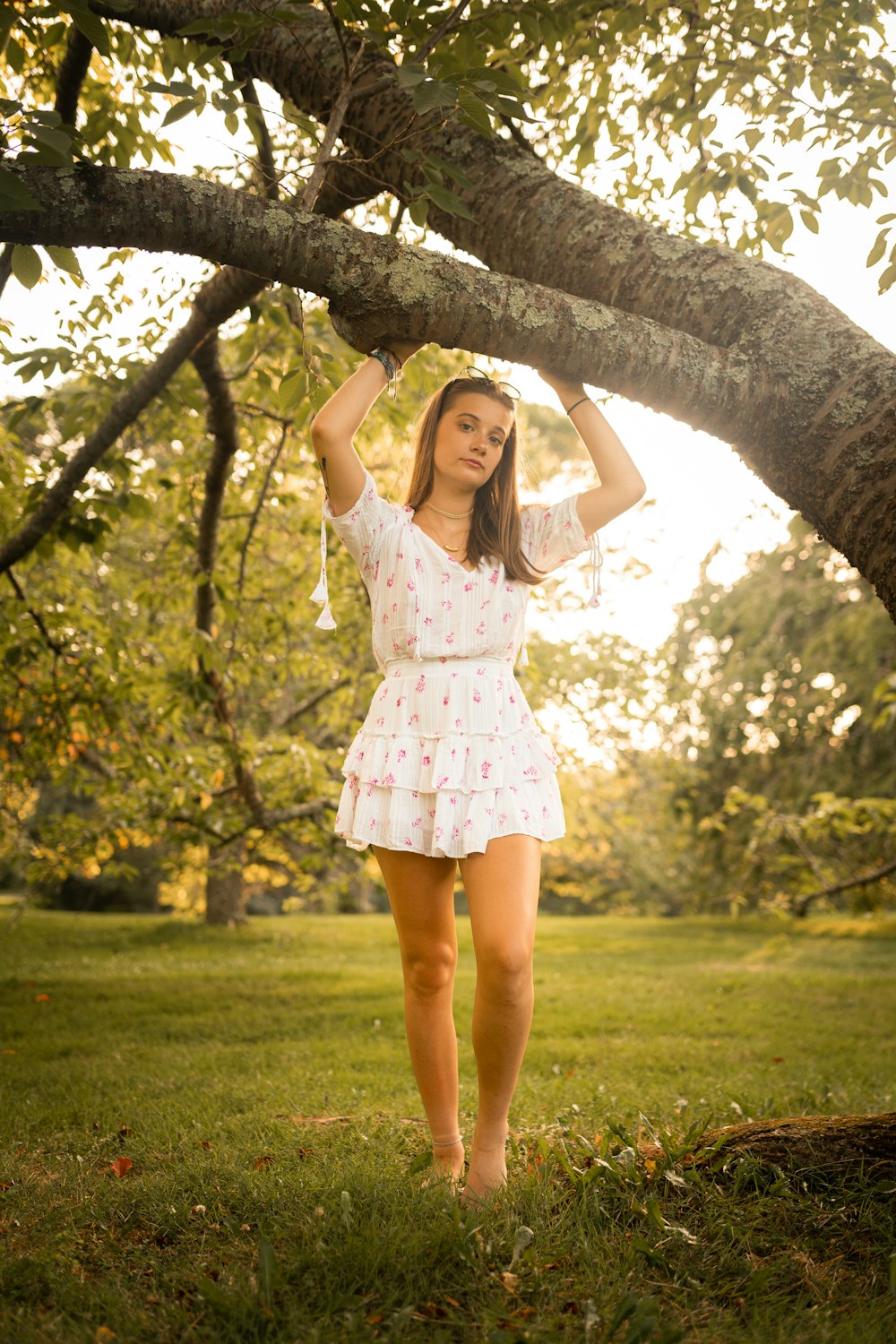 girl in white and pink floral dress standing on tree branch during daytime