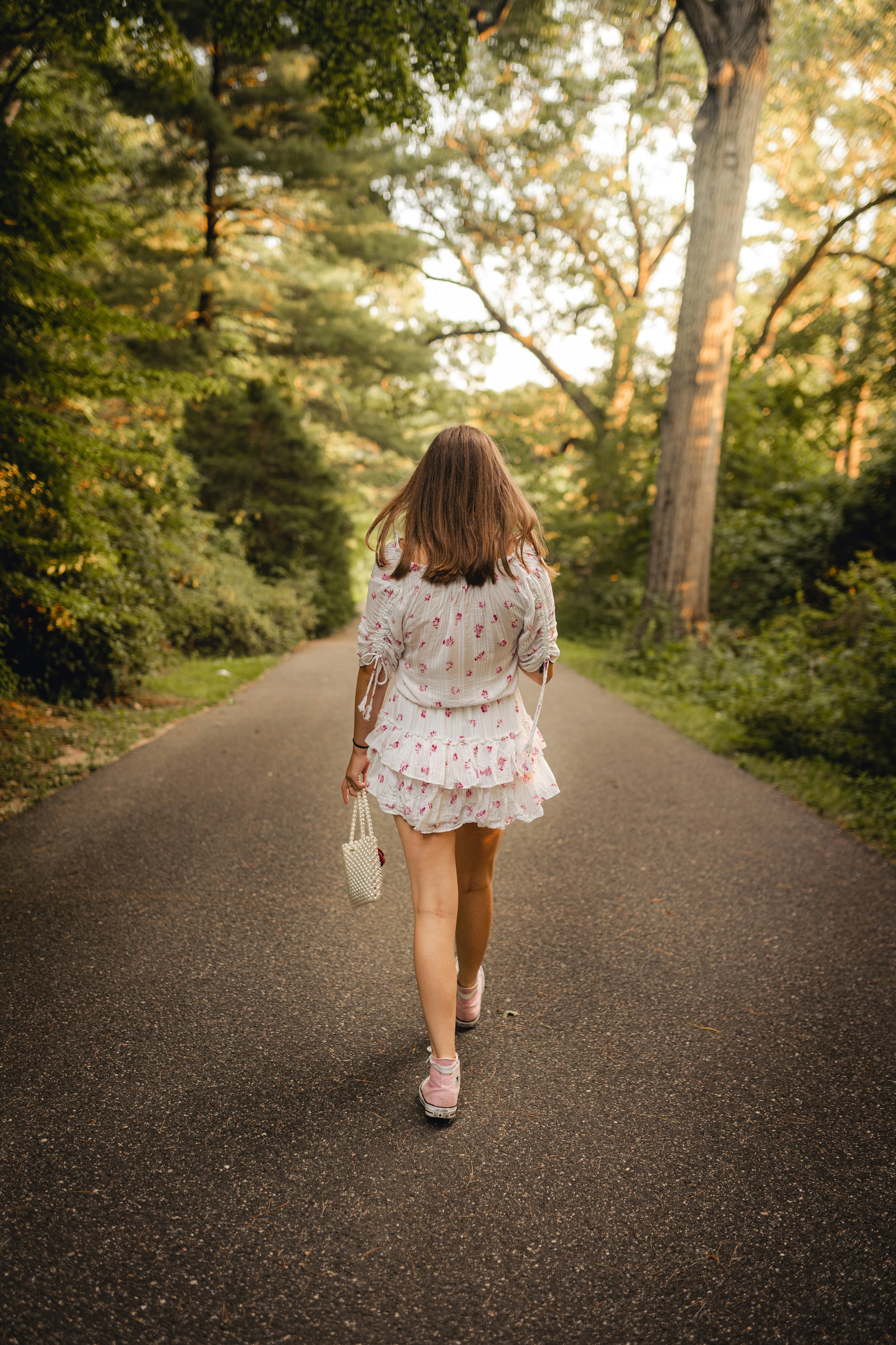 girl in white and pink floral dress walking on gray asphalt road during daytime