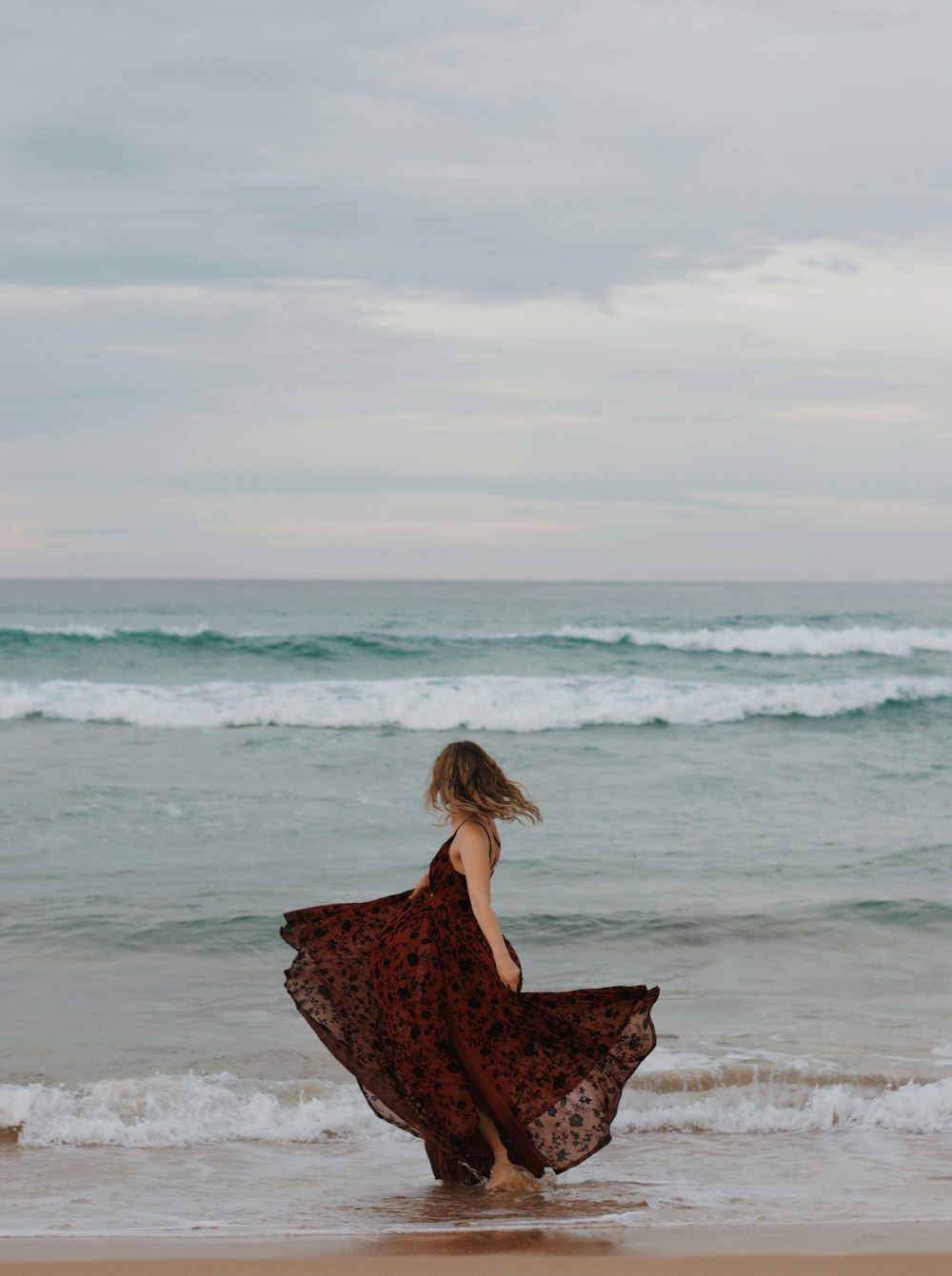 昼間、海岸に立つ黒と赤の花柄のドレスを着た女性
