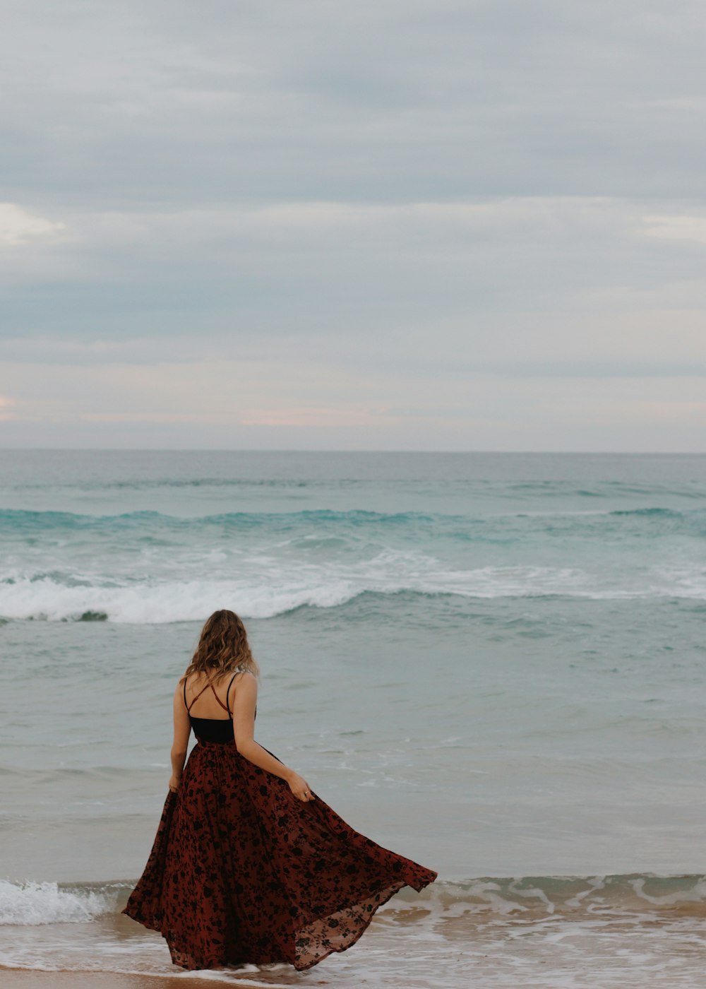 낮 동안 해변에 서 있는 검은색과 갈색 꽃 드레스를 입은 여자