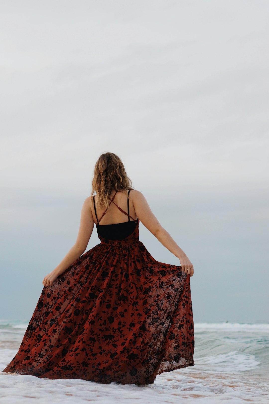 woman in black and red spaghetti strap dress standing on beach during daytime