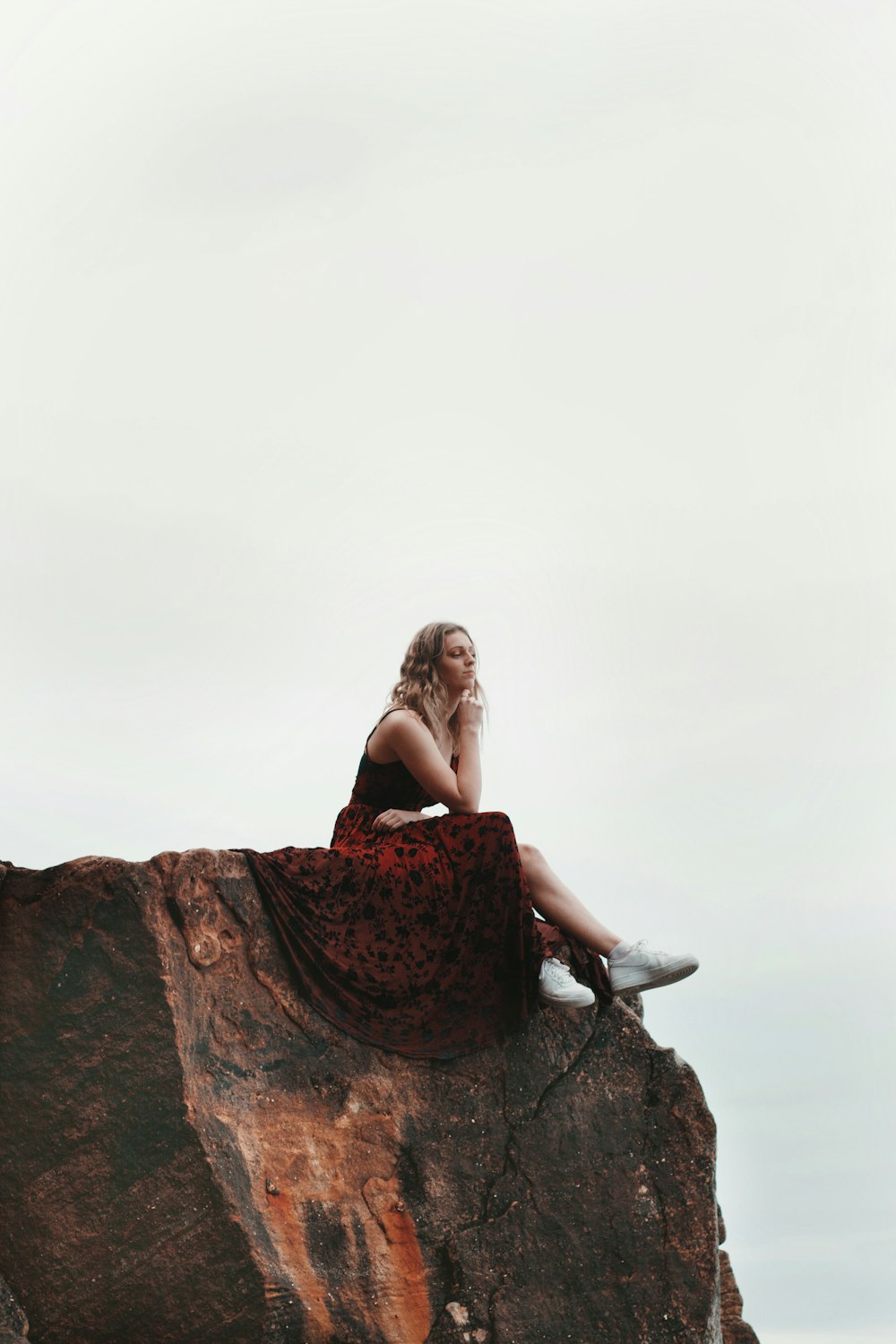 Donna in abito floreale nero e rosso che si siede sulla roccia