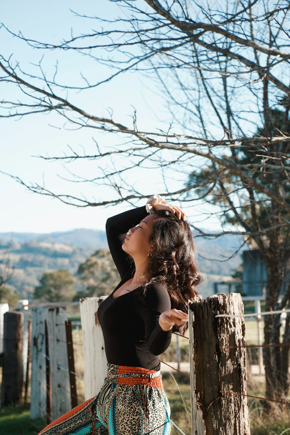 woman in black tank top and black pants sitting on brown wooden fence during daytime
