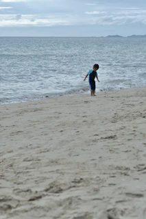 A child playing with a beach ball while waves gently lap at their feet