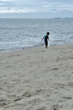 A child playing with a beach ball while waves gently lap at their feet