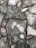 A close-up view of a patterned stone pavement with irregularly shaped stones fitted together. The stones vary in shades of gray and brown, with visible natural textures and weathering. Dark lines of grout fill the gaps between the stones.