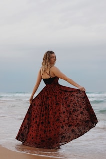 woman in red and black spaghetti strap dress standing on beach during daytime