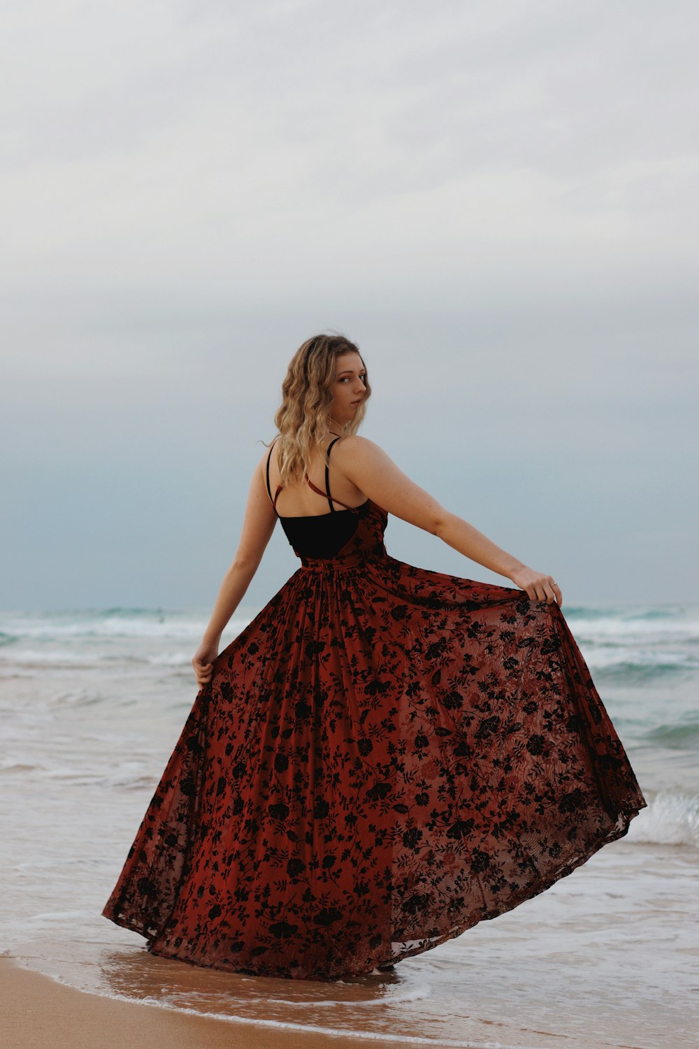woman in red and black spaghetti strap dress standing on beach during daytime