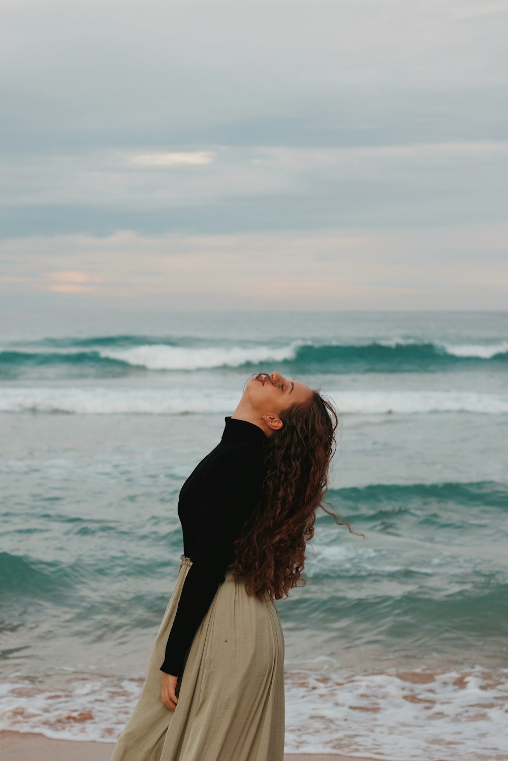 Femme en chemise à manches longues noire debout sur le bord de mer pendant la journée