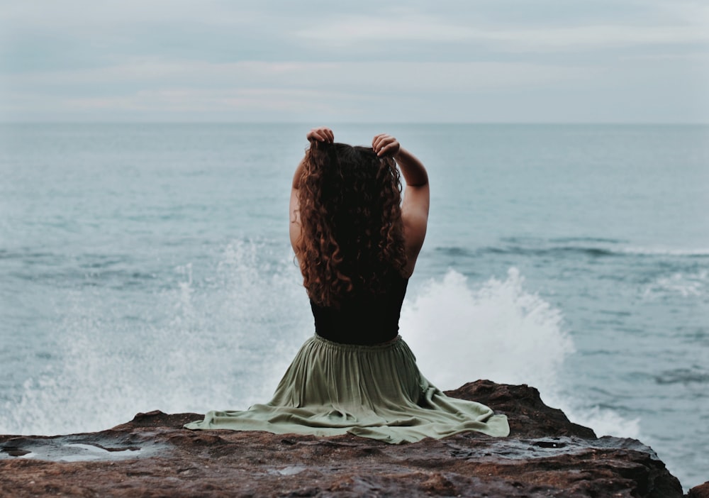 donna in vestito bianco che si siede sulla roccia vicino al mare durante il giorno