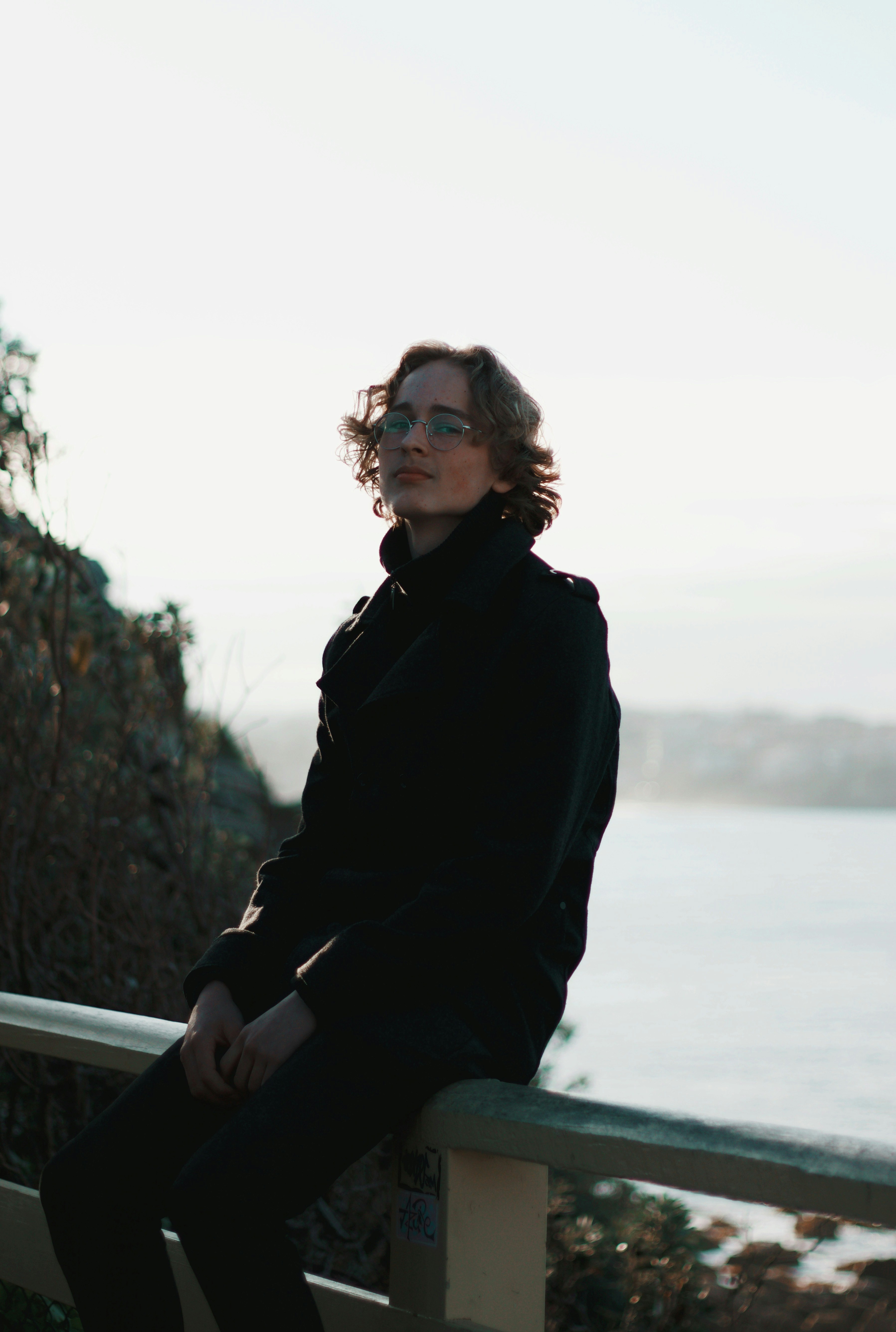 woman in black jacket sitting on white metal railings during daytime