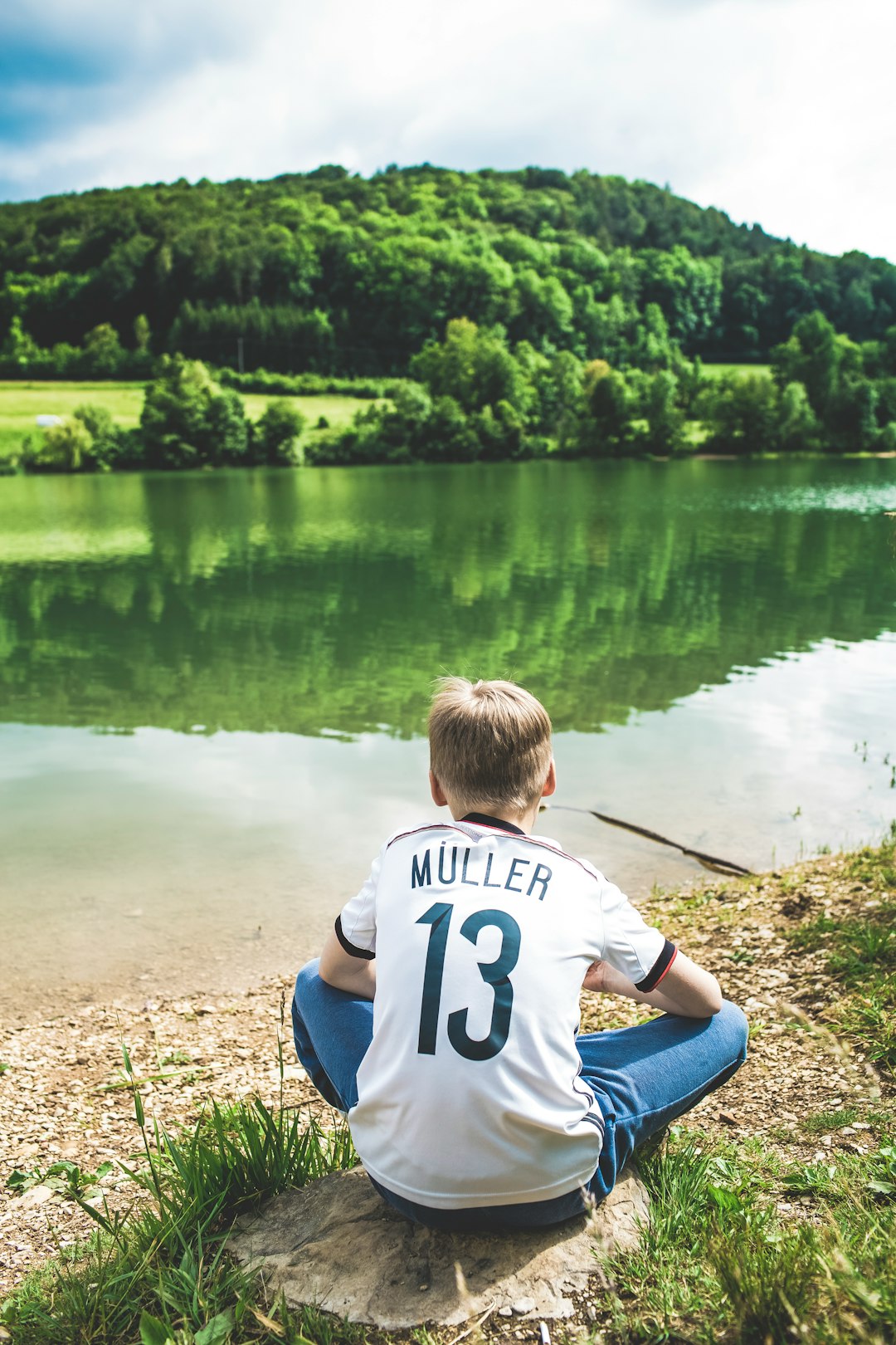 boy in white and blue shirt sitting on blue chair near lake during daytime