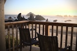 Sunlit holiday apartment balcony with comfortable chairs and panoramic coastal views.